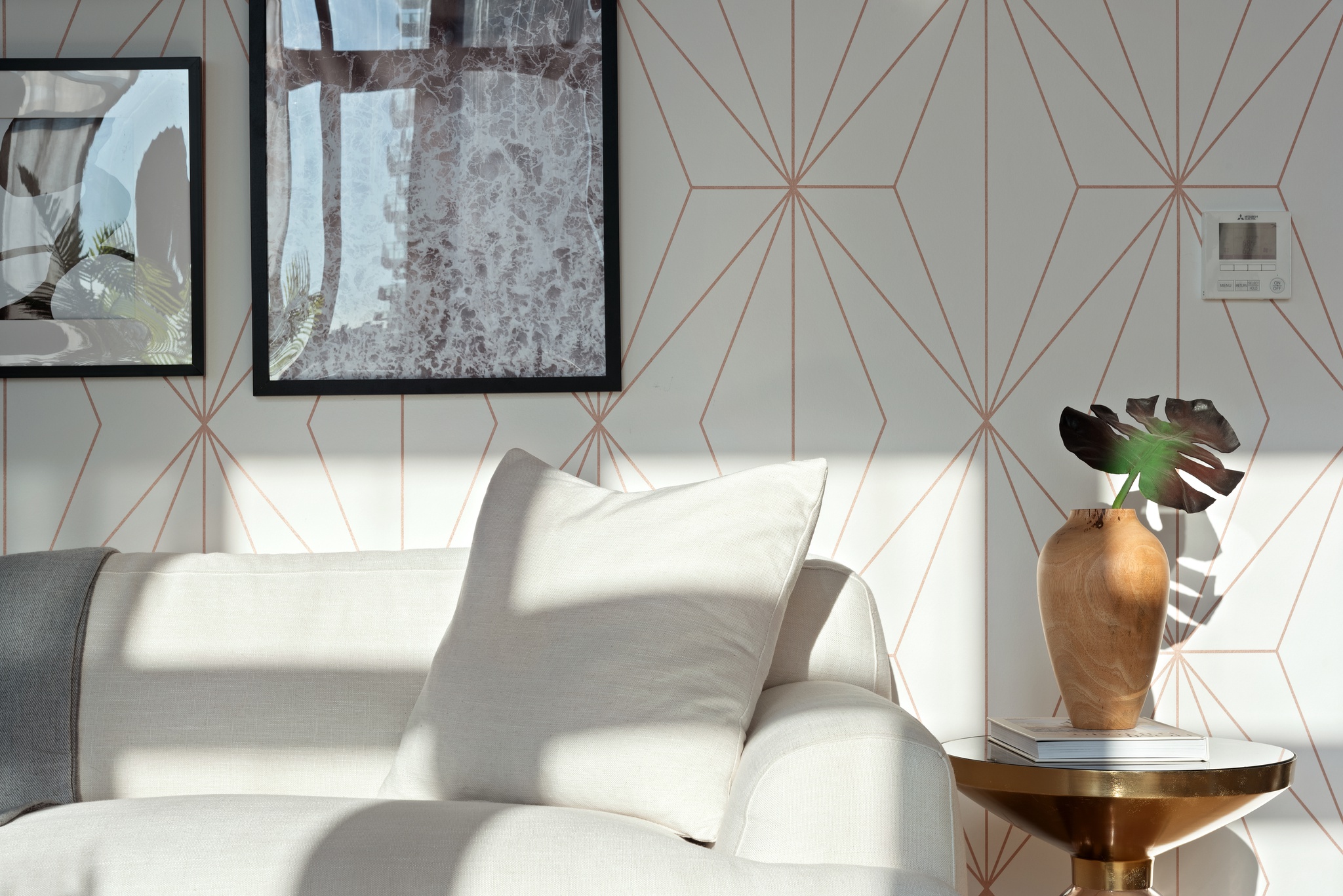 Close up view of corner of white couch in living room with side table with plant on book, white throw pillow, grey throw blanket, wallpaper accent wall with framed photography