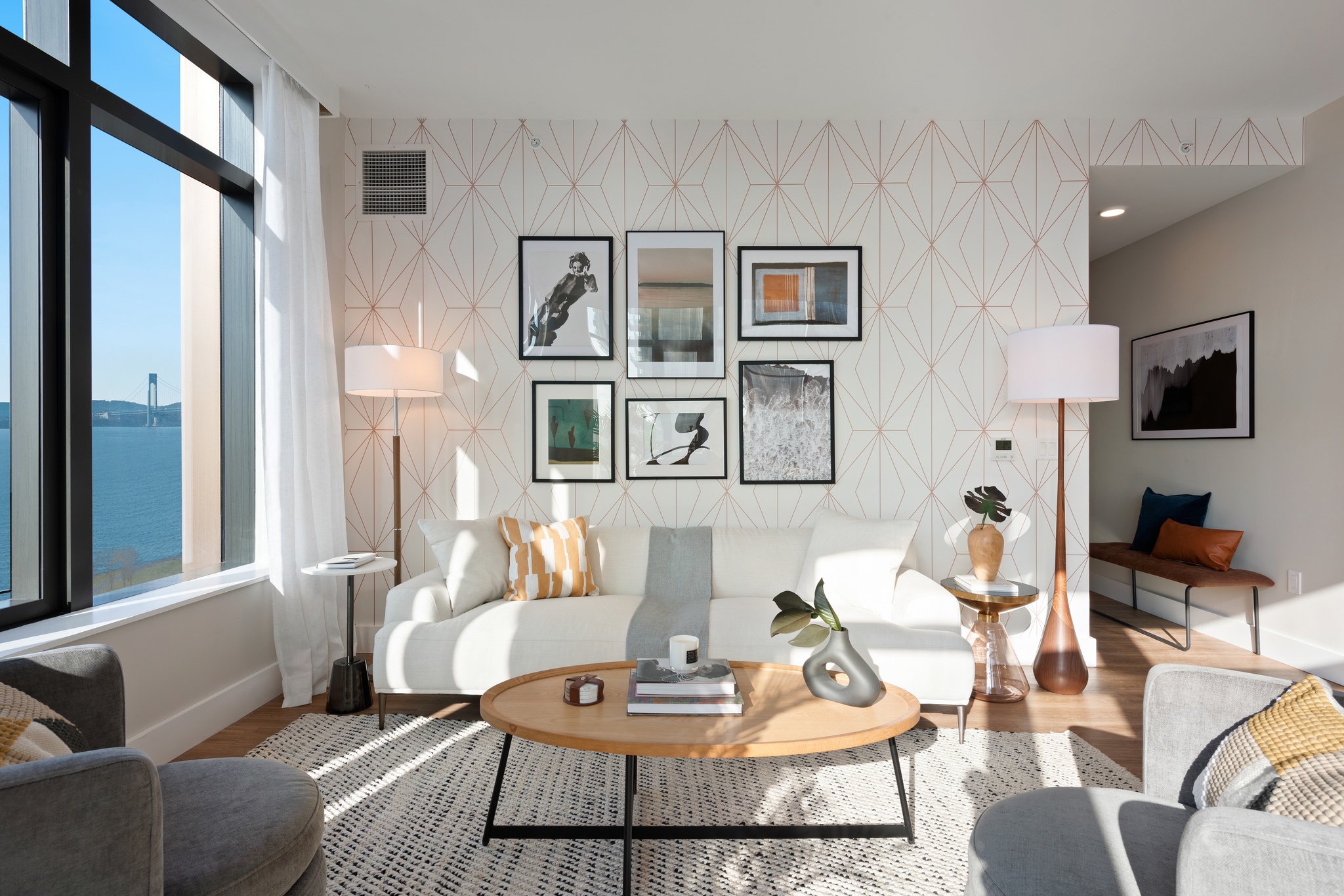 View of white couch in bright living room with area rug, wood coffee table with books and plants, modern photography on modern wallpaper accent wall behind couch