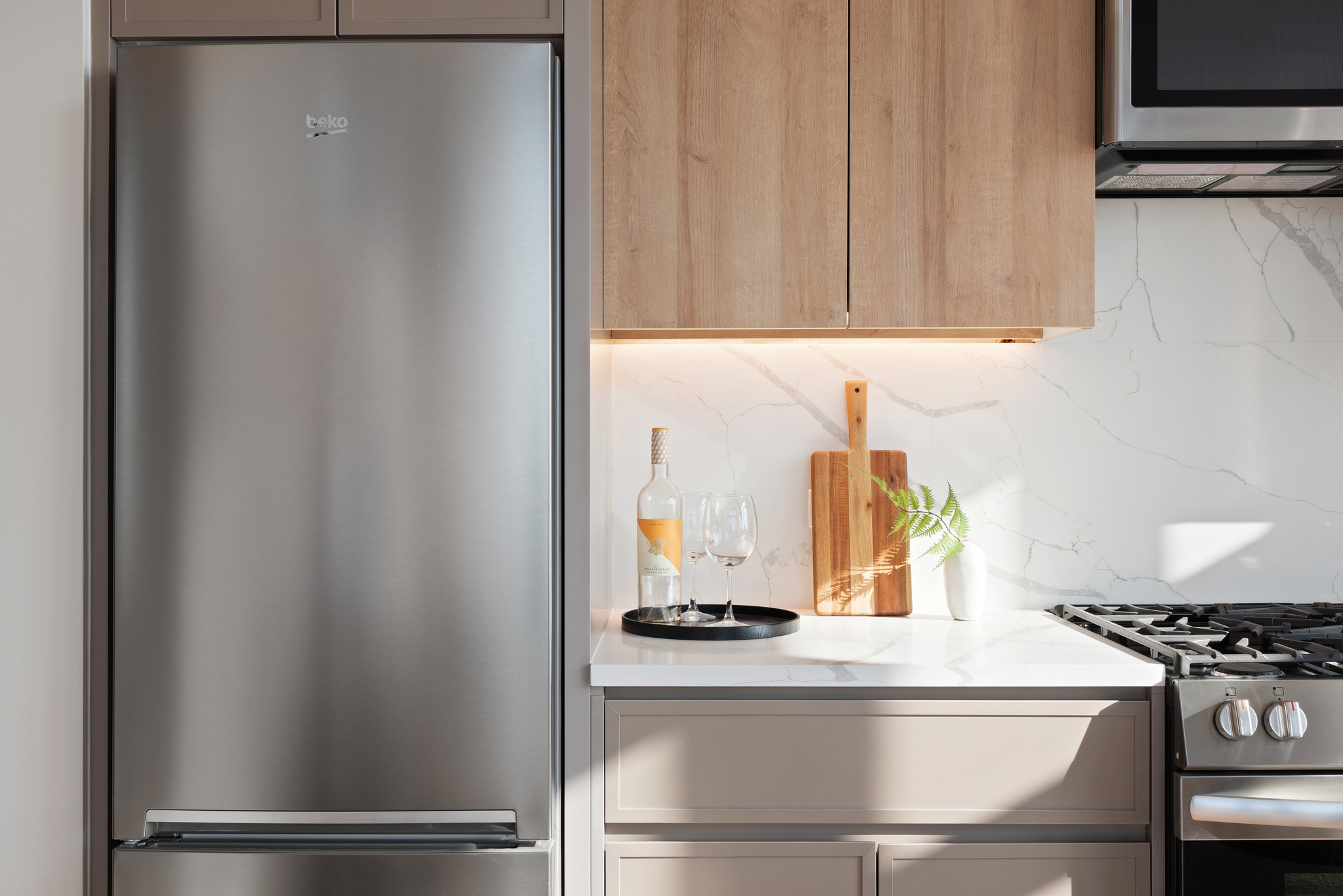 Kitchen detail showing light wood and light grayish cabinetry, white marble looking backsplash, stainless steel fridge and stove/oven/microwave combo