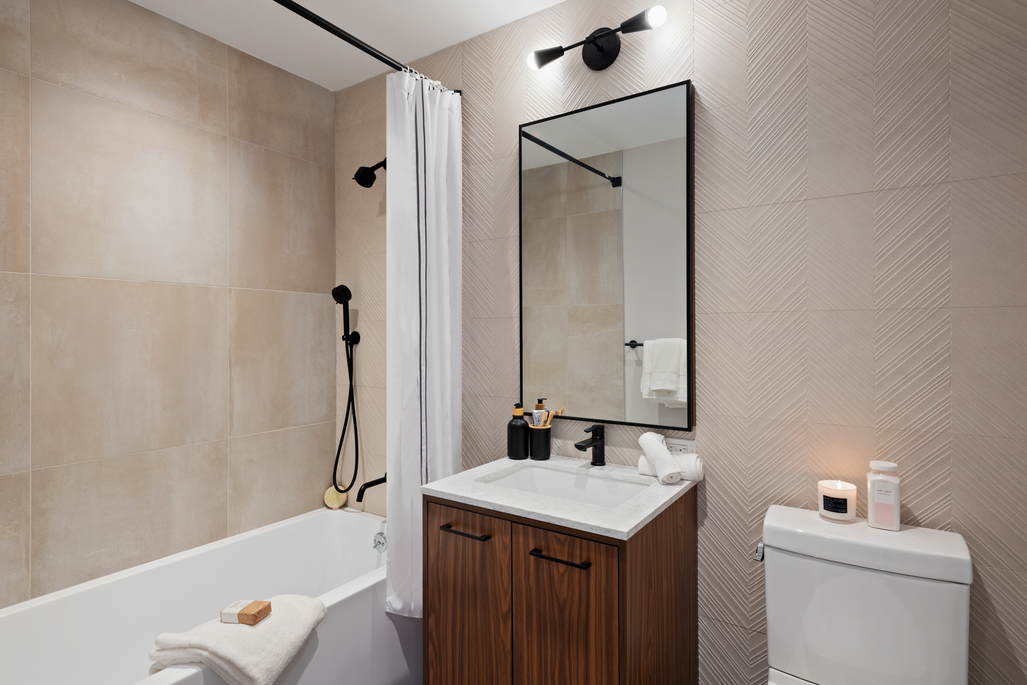 Modern bathroom with wood vanity and white sink and vertical rectangle mirror above, white tub with large beige tiles in shower and textured tiles on walls